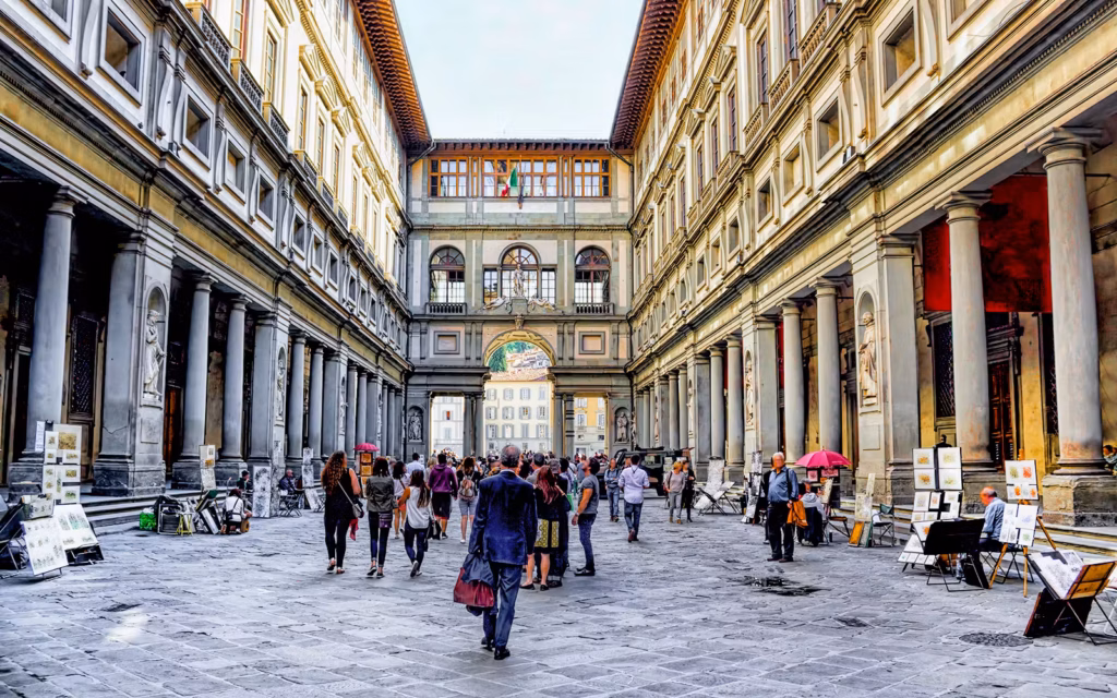 Uffizi Gallery courtyard in Florence, Italy, with tourists and art stalls.
